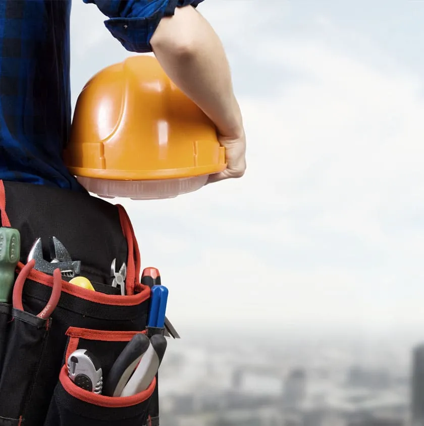 A tradesperson holding a hard hat and tool belt